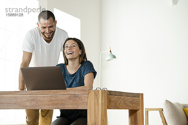 Glückliches Paar arbeitet von zu Hause am Laptop im Home-Office im modernen Wohnzimmer