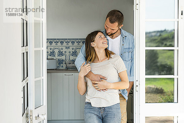 Attraktives junges Paar steht zu Hause zusammen in der Tür und lächelt sich an