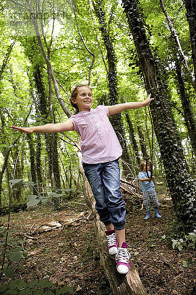 Mädchen balanciert auf Baumstamm im Wald
