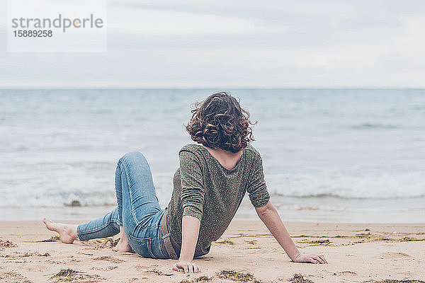 Junge Frau sitzt am Strand und schaut auf das Meer