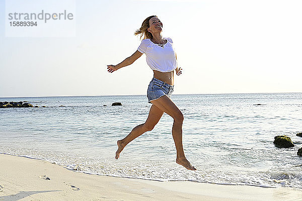 Schöne Frau rennt und springt vor Freude am Strand