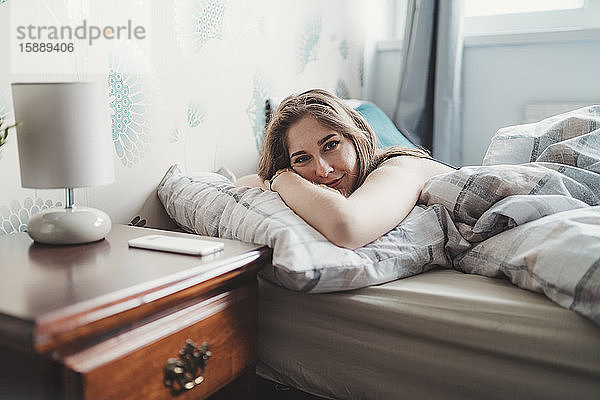 Porträt einer selbstbewussten  attraktiven jungen Frau  die zu Hause im Bett liegt