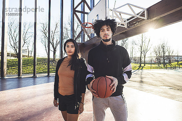 Porträt eines jungen Mannes und einer jungen Frau auf einem Basketballplatz im Gegenlicht