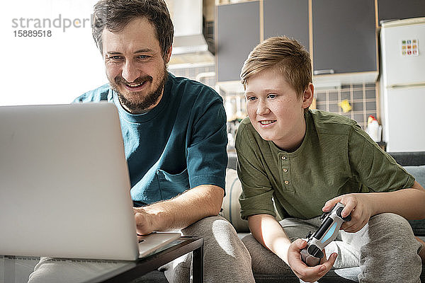 Porträt von Vater und Sohn  die zusammen auf der Couch sitzen und ein Computerspiel spielen