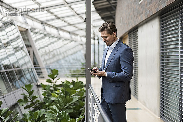 Geschäftsmann mit Smartphone im grünen Atrium