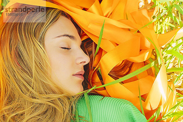 Bildnis einer jungen Frau mit geschlossenen Augen in einem Feld mit orangefarbenen Bändern liegend