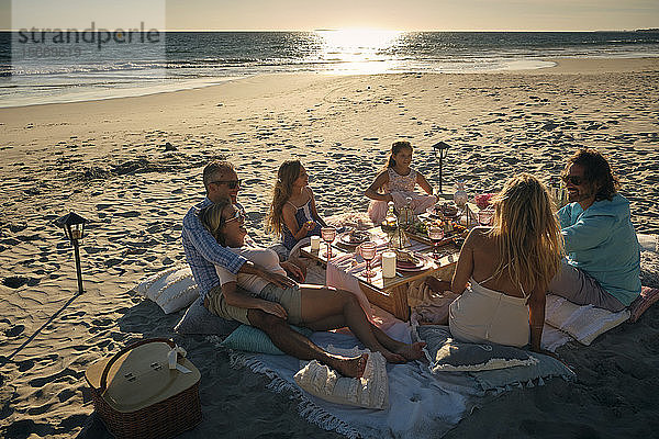 Familie und Freunde genießen ein Picknick  während sie bei Sonnenuntergang am Strand sitzen. Riviera Nayarit  Mexiko