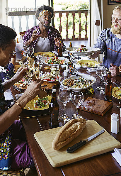 Multiethnische Freunde essen zu Mittag  während sie am Esstisch im Raum sitzen
