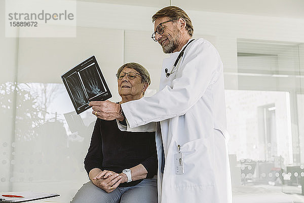 Arzt bespricht Röntgenbild einer gebrochenen Hand mit älterem Patienten