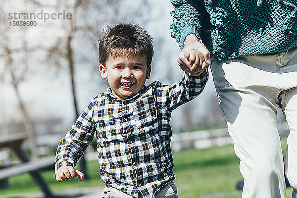 Porträt eines glücklichen kleinen Jungen  der Hand in Hand mit seiner Mutter in einem Park läuft