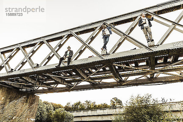 Drei Männer mit Bierflaschen auf einer alten Eisenbahnbrücke