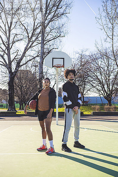 Porträt eines jungen Mannes und einer jungen Frau auf einem Basketballplatz stehend