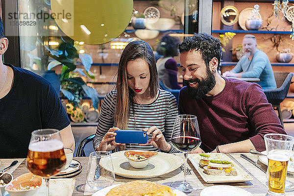 Frau macht Smartphone-Fotos von Lebensmitteln bei einem Abendessen mit Freunden in einem Restaurant