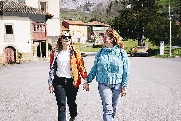 Zwei glückliche Frauen mit Rucksäcken  die Hand in Hand spazieren gehen  Stausee Valdemurio  Asturien  Spanien
