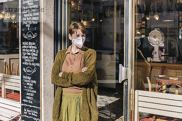 Frau mit Maske vor ihrem geschlossenen Restaurant stehend
