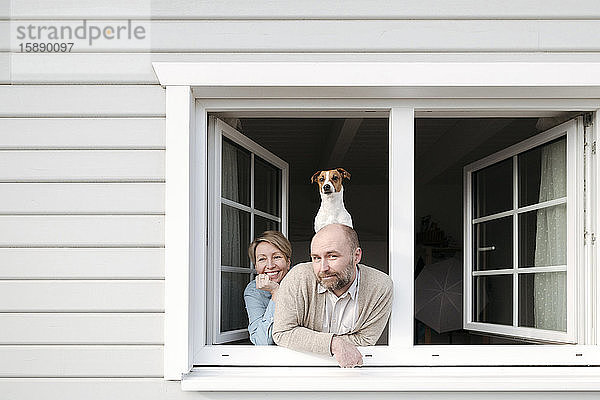 Ehepaar mit Hund lehnt sich aus dem Fenster ihres Hauses