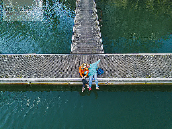 Zwei glückliche Freunde sitzen Seite an Seite auf dem Bootssteg  Valdemurio-Stausee  Asturien  Spanien