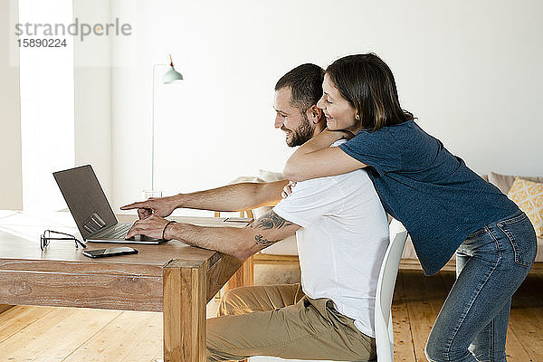 Lächelndes Paar bei der Arbeit am Laptop von zu Hause im Home-Office im modernen Wohnzimmer
