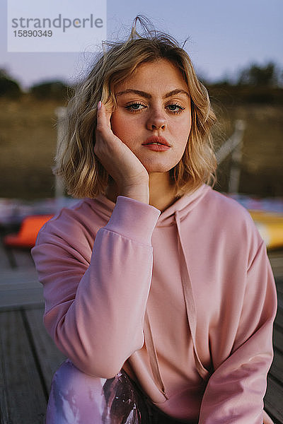 Porträt einer jungen blonden Frau mit rosa Kapuzenpullover auf dem Steg