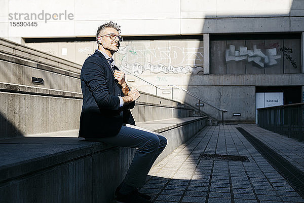 Grauhaariger Geschäftsmann sitzt auf einer Treppe im Freien