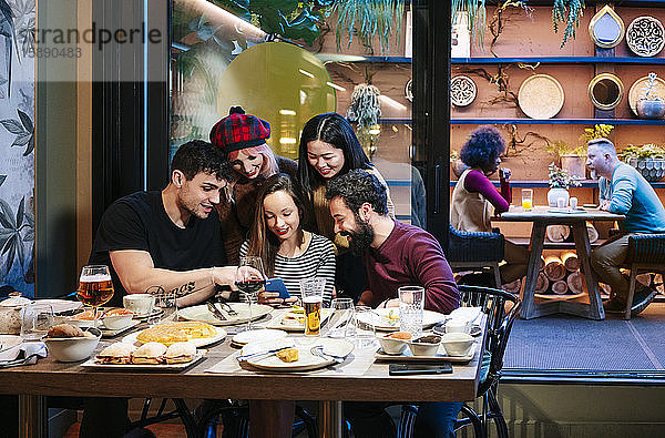 Freunde beim Abendessen in einem schicken Restaurant mit Blick auf das Smartphone