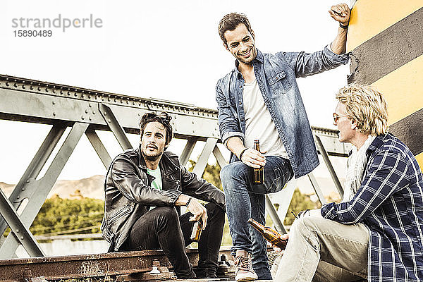 Drei Männer trinken Bier auf einer alten Eisenbahnbrücke