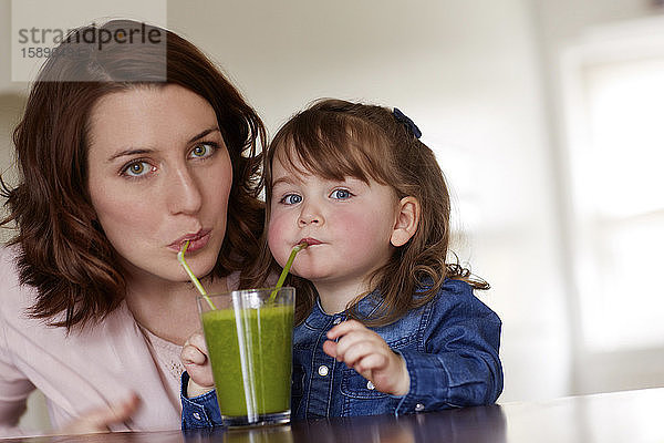 Porträt einer jungen Mutter und einer kleinen Tochter  die zusammen grünen Smoothie trinken