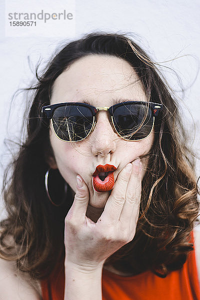 Porträt einer jungen Frau mit roten Lippen und Sonnenbrille  die mit dem Mund schmollt