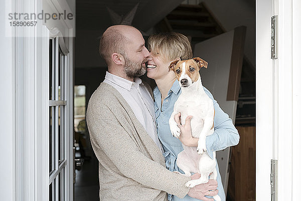 Glückliches Paar mit Hundeküssen am Eingang ihres Hauses