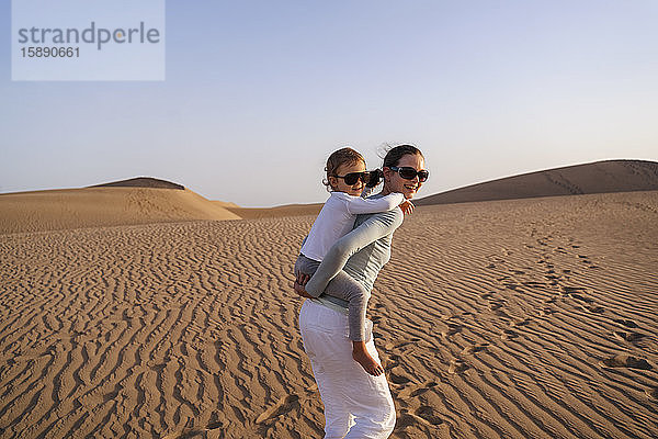 Mutter trägt Tochter huckepack in Sanddünen  Gran Canaria  Spanien