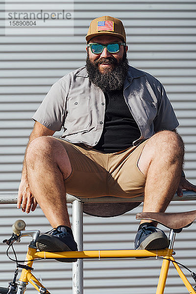 Bildnis eines bärtigen Mannes mit Fixie-Fahrrad auf einem Geländer sitzend