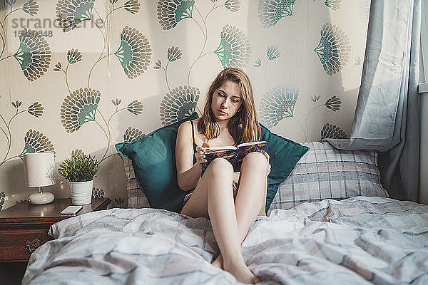 Attraktive junge Frau sitzt zu Hause im Bett mit einem Buch