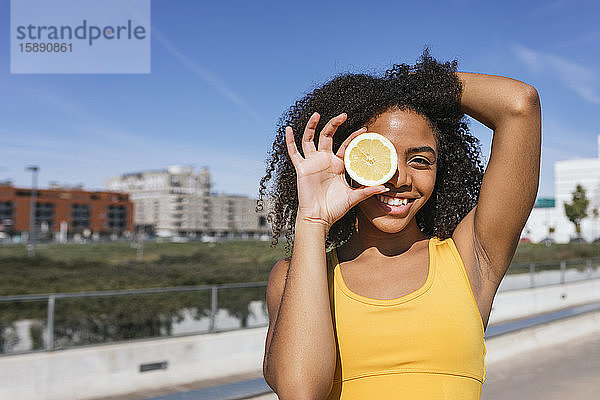 Porträt einer lachenden jungen Frau  die das Auge mit einer Zitronenhälfte bedeckt