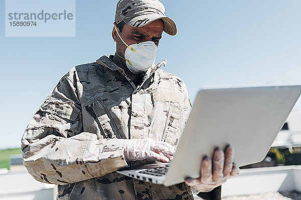 Soldat mit Gesichtsmaske bei Notfalleinsatz  mit Laptop