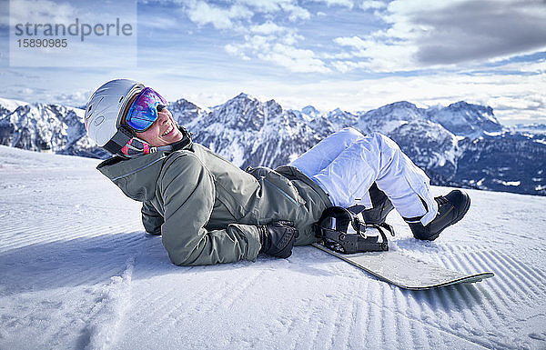 Lächelnde Frau sitzt mit Snowboard auf dem Aussichtspunkt und schaut in die Kamera