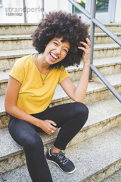 Porträt einer lachenden jungen Frau  die im Freien auf einer Treppe sitzt