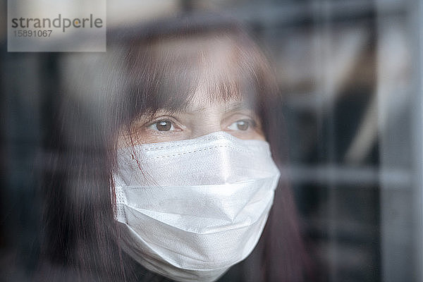 Porträt von älteren Frauen  die zu Hause eine Maske tragen und aus dem Fenster schauen