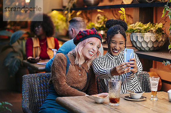 Zwei Freundinnen sitzen im Restaurant und nehmen sich ein Smartphone