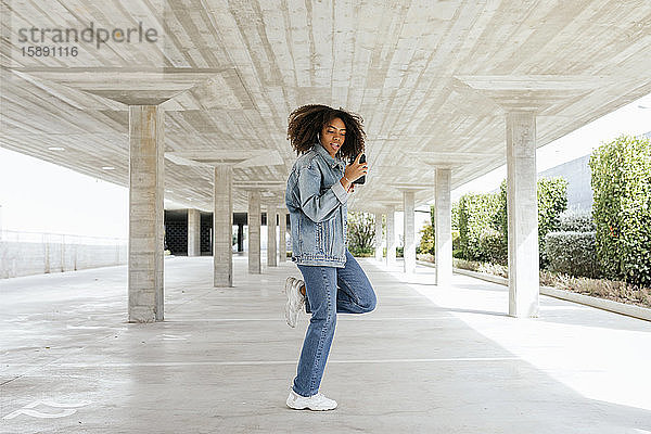 Junge Frau tanzt  während sie mit Kopfhörern und Smartphone Musik hört