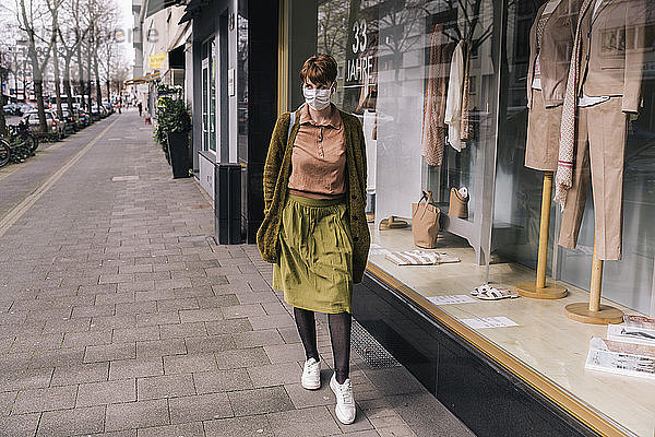Frau mit Maske geht an einem Bekleidungsgeschäft in der Stadt entlang