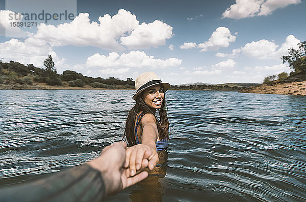 Porträt einer glücklichen jungen Frau  die in einem See badet und die Hand ihres Freundes hält