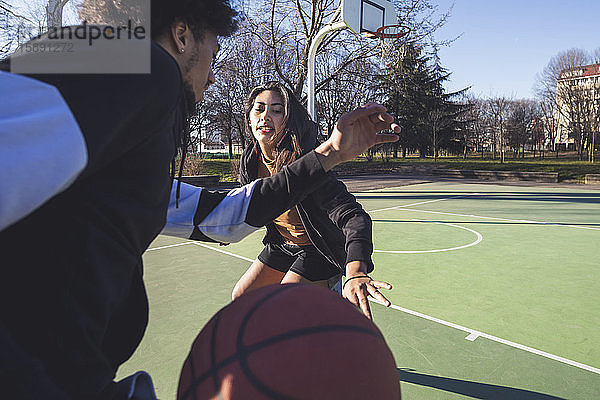 Junger Mann und Frau spielen Basketball auf dem Platz