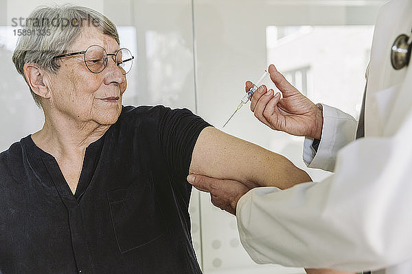 Arzt injiziert Impfstoff in den Arm eines älteren Patienten