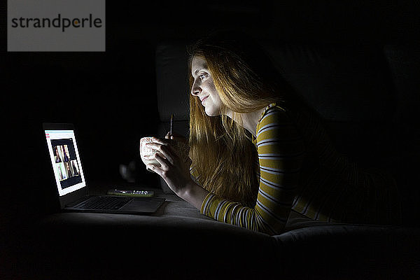 Junge Frau mit einer Laptop-Videokonferenz auf der Couch zu Hause beim Abendessen