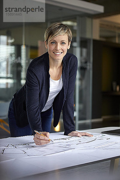 Porträt einer lächelnden Frau  die im Büro an einem Bauplan arbeitet