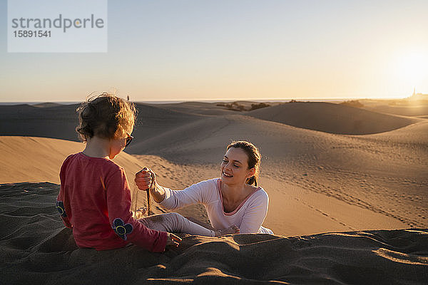 Mutter und Tochter spielen bei Sonnenuntergang mit Sand in den Dünen  Gran Canaria  Spanien