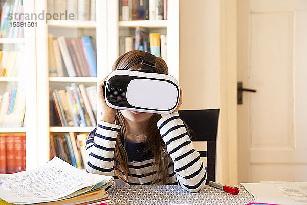 Mädchen  das zu Hause am Tisch sitzt und eine Virtual-Reality-Brille benutzt