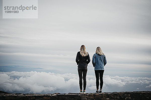 Rückansicht von Freundinnen  die auf idyllische Wolkenlandschaft blicken  während sie am Vulkan Haleakala stehen  Hawaii  Maui  USA