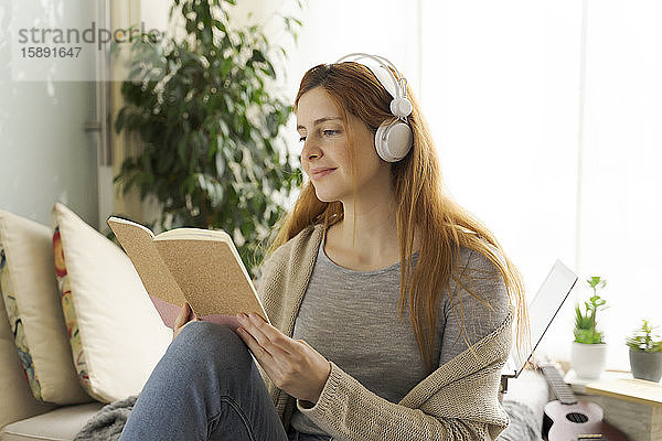 Junge Frau mit Kopfhörern und Leseheft zu Hause