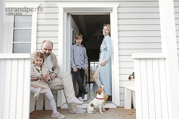 Glückliche Familie mit Katze und Hund auf der Veranda ihres Hauses